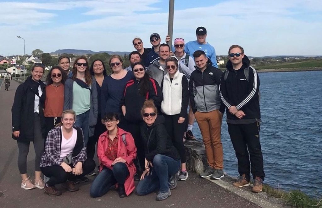 A group of people, perhaps friends on a study abroad journey, pose for a photo outdoors by the water on a sunny day, capturing memories that are as priceless as financial resources.